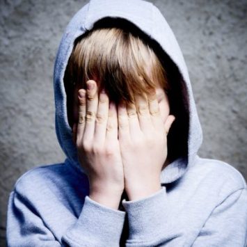 Boy in hoodie covering face, representing toxic masculinity