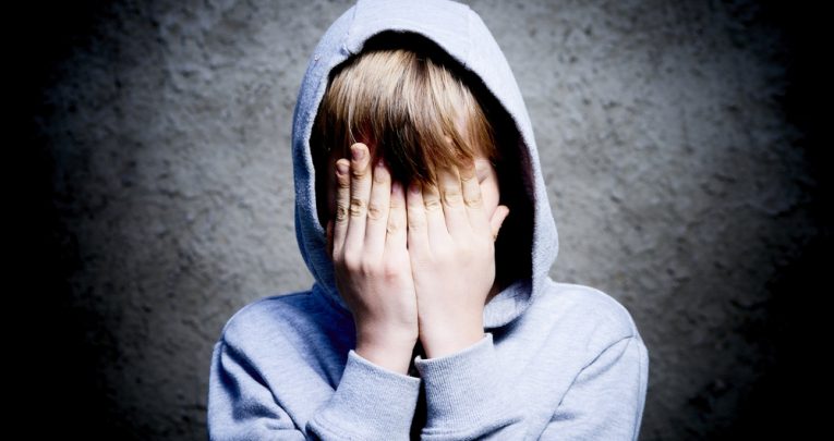 Boy in hoodie covering face, representing toxic masculinity