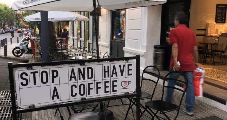 Sign outside cafe saying "Stop and have a coffee", representing persuasive writing techniques