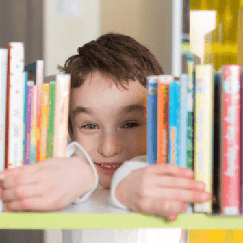 Boy peeking through gap in bookshelf