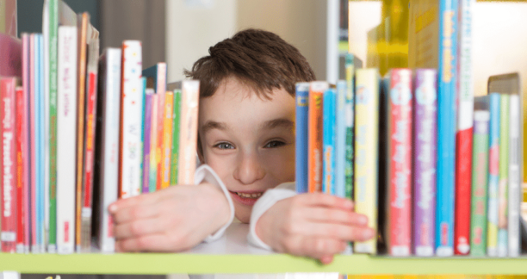 Boy peeking through gap in bookshelf