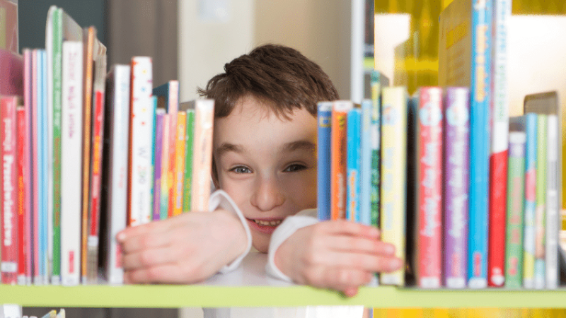 Boy peeking through gap in bookshelf
