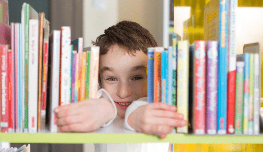 Boy peeking through gap in bookshelf