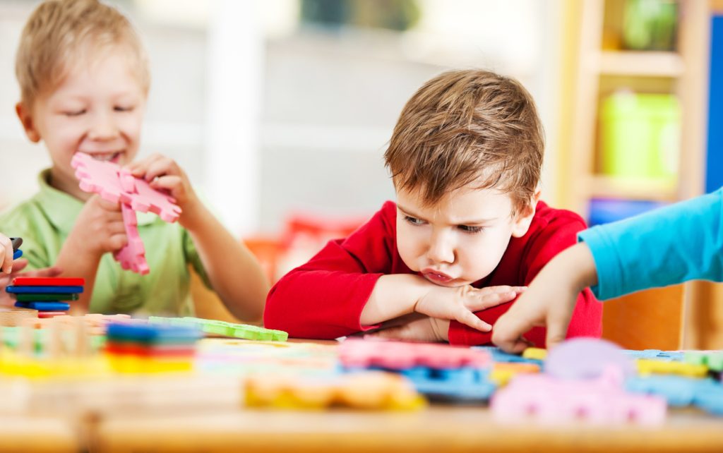 Young boy looking angry at a school table, surrounded by foam blocks