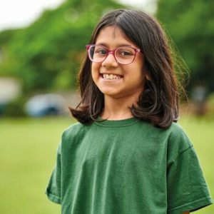 Girl in green t-shirt and pink glasses, smiling