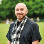 Man in black t-shirt and black-and-white scarf smiling