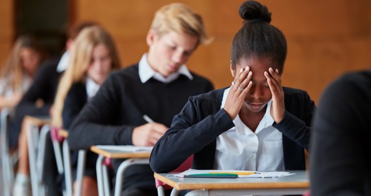 Teenage girl in school exam hall holds her head in her hands