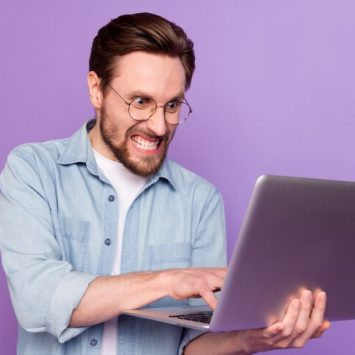 Angry adult man holding laptop and typing