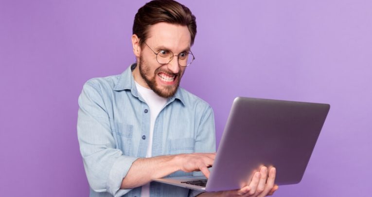 Angry adult man holding laptop and typing