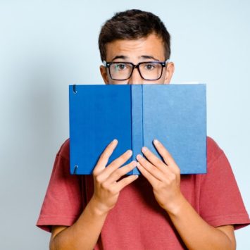 Bespectacled boy holding up book that partially conceals his face