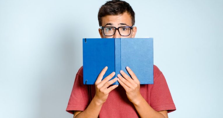 Bespectacled boy holding up book that partially conceals his face