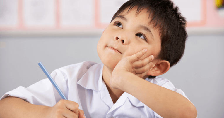 Young boy with black hair and white shirt looking upwards and holding a pencil