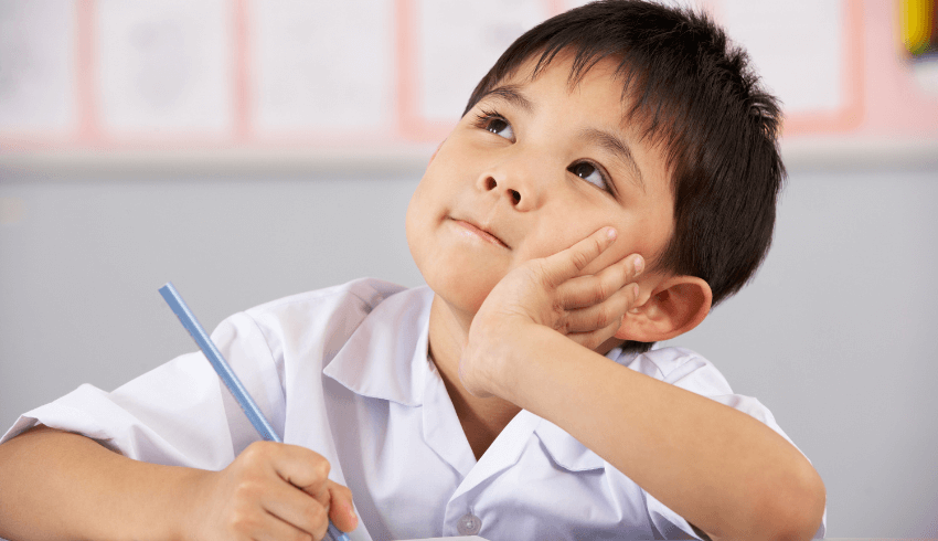 Young boy with black hair and white shirt looking upwards and holding a pencil