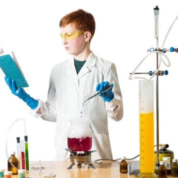 Photo of a young boy reading a book while conducting a science experiment to illustrate the concept of cross-curricular literacy