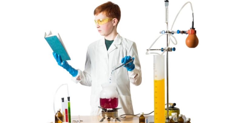 Photo of a young boy reading a book while conducting a science experiment to illustrate the concept of cross-curricular literacy