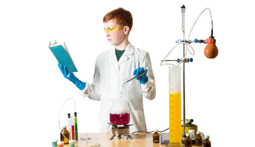Photo of a young boy reading a book while conducting a science experiment to illustrate the concept of cross-curricular literacy