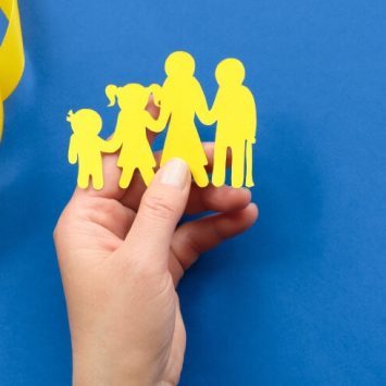 Hand holding a yellow paper cutout representing a family, against a blue background