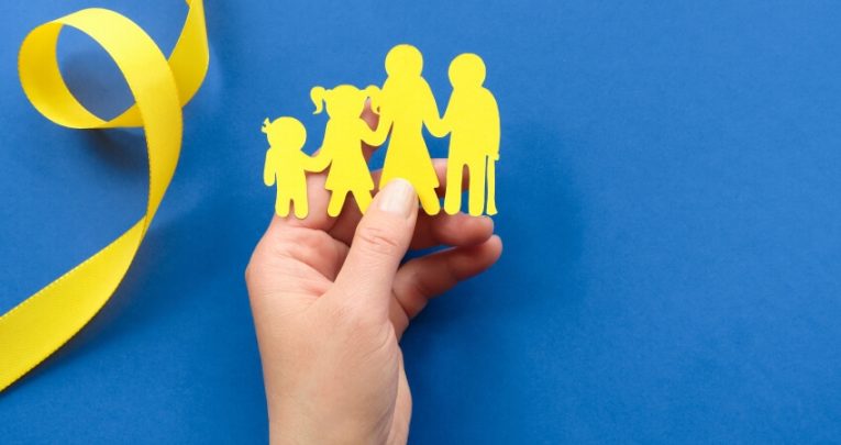 Hand holding a yellow paper cutout representing a family, against a blue background