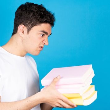 Frustrated-looking boy holding several books in his hands