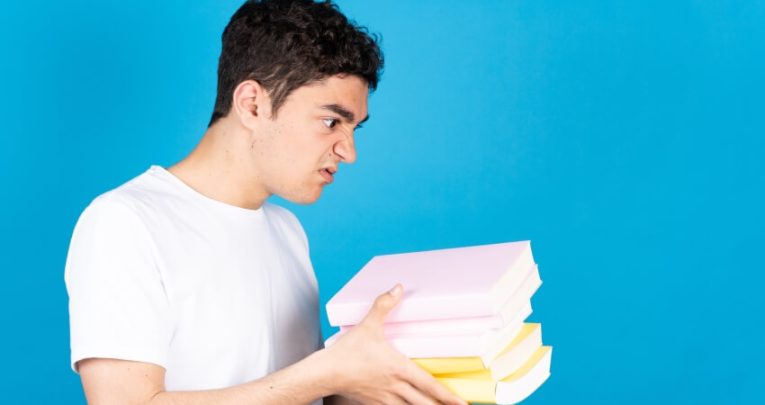 Frustrated-looking boy holding several books in his hands