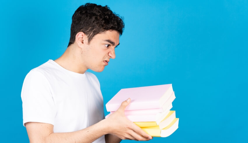 Frustrated-looking boy holding several books in his hands