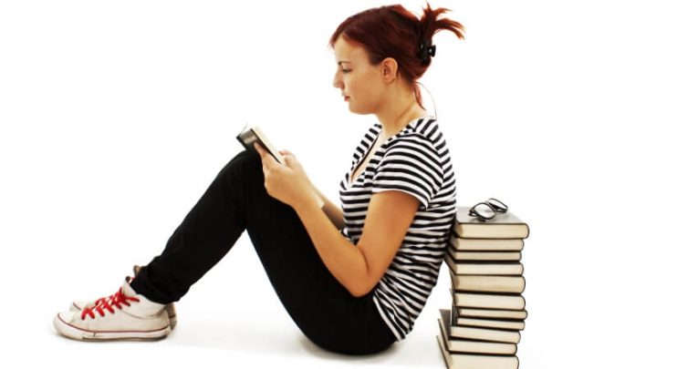 Teenage girl reading and leaning against a stack of books