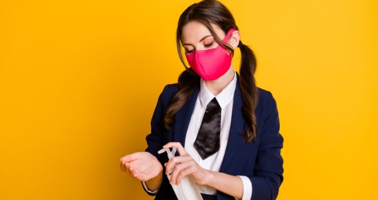 Photo of teenage girl in school uniform wearing medical mask and applying hand sanitiser