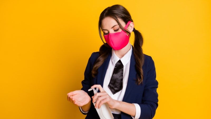 Photo of teenage girl in school uniform wearing medical mask and applying hand sanitiser