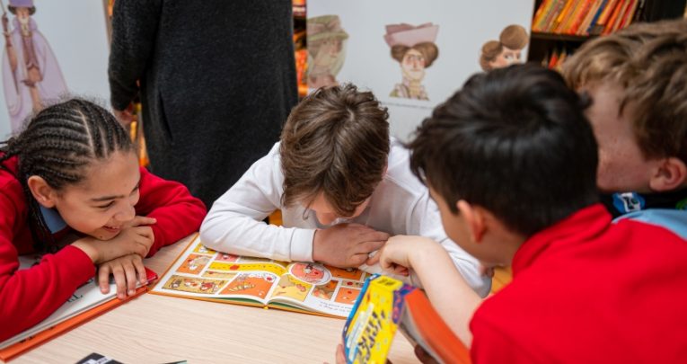 primary age children shown in classroom engaged in a reading activity