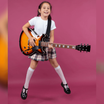 Girl in school uniform jumping with electric guitar. Pink background.