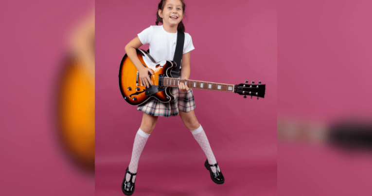 Girl in school uniform jumping with electric guitar. Pink background.