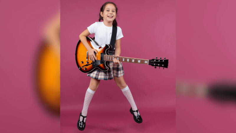Girl in school uniform jumping with electric guitar. Pink background.