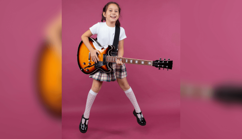 Girl in school uniform jumping with electric guitar. Pink background.