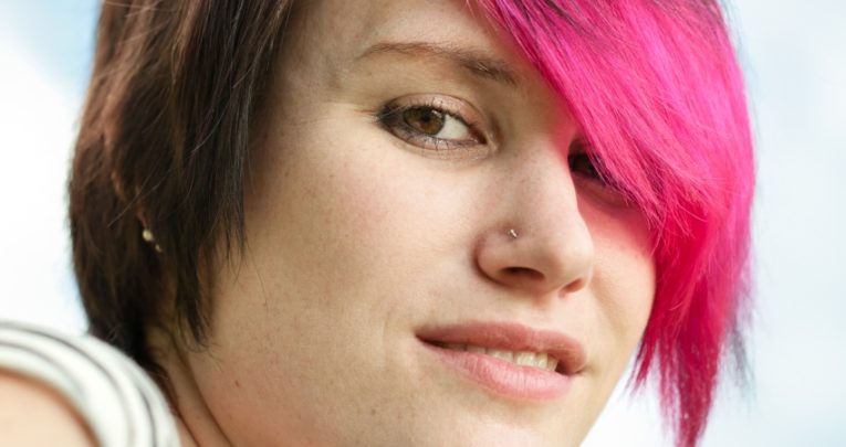 CLose up on teen with pink hair and a nose stud, conveying contravention of school uniform rules