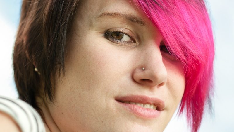 CLose up on teen with pink hair and a nose stud, conveying contravention of school uniform rules