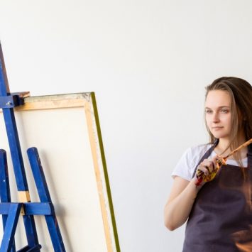 A female student pictured holding a paintbrush in front of an eisel