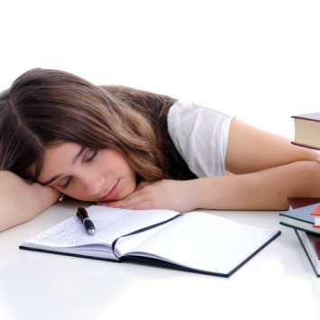 Photo of a lethargic and tired-looking female student surrounded by textbooks