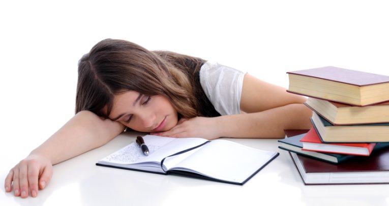 Photo of a lethargic and tired-looking female student surrounded by textbooks