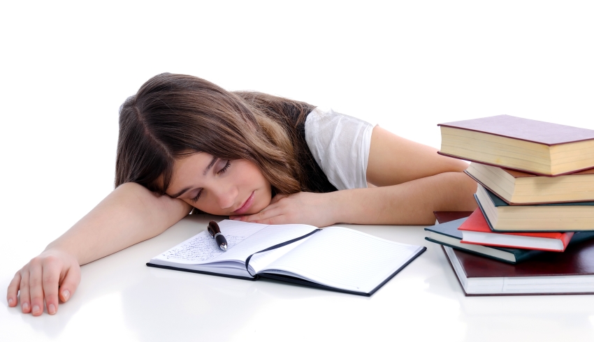Photo of a lethargic and tired-looking female student surrounded by textbooks