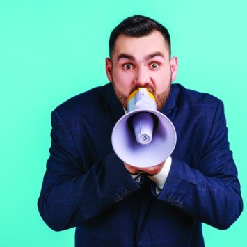 Photograph of a besuited man talking into a loudhailer