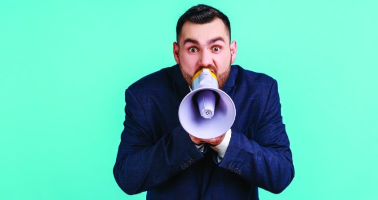 Photograph of a besuited man talking into a loudhailer