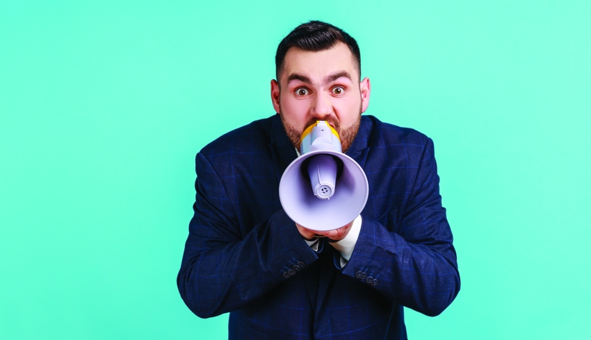 Photograph of a besuited man talking into a loudhailer