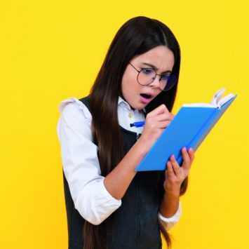 Photo of young teenager looking surprised as she writes in a notebook