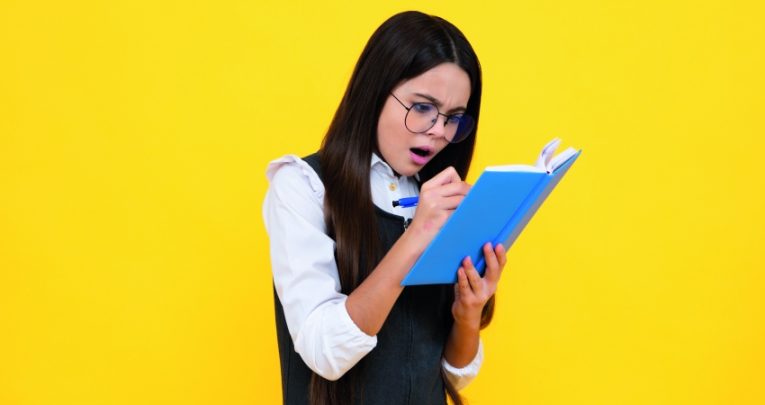 Photo of young teenager looking surprised as she writes in a notebook