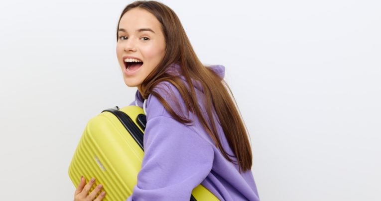 Photo of excited teenage girl carrying a suitcase