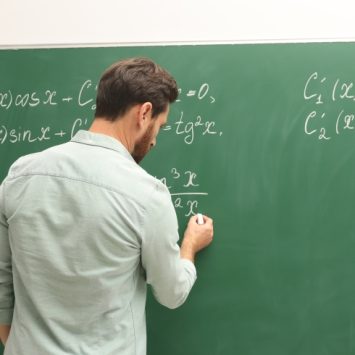 male teacher writes maths equations on a chalkboard