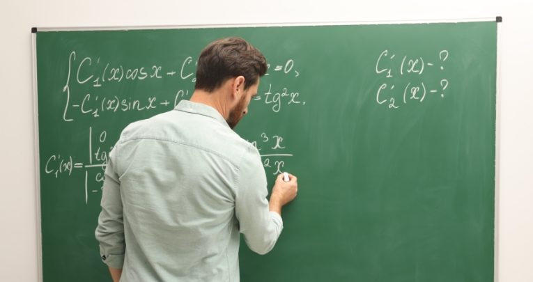 male teacher writes maths equations on a chalkboard