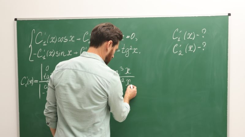 male teacher writes maths equations on a chalkboard