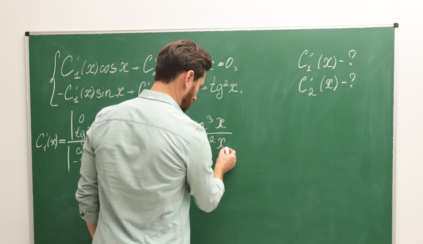 male teacher writes maths equations on a chalkboard