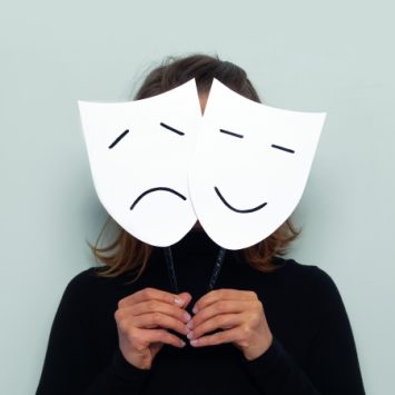 Photograph of figure concealed behind comedy and tragedy masks